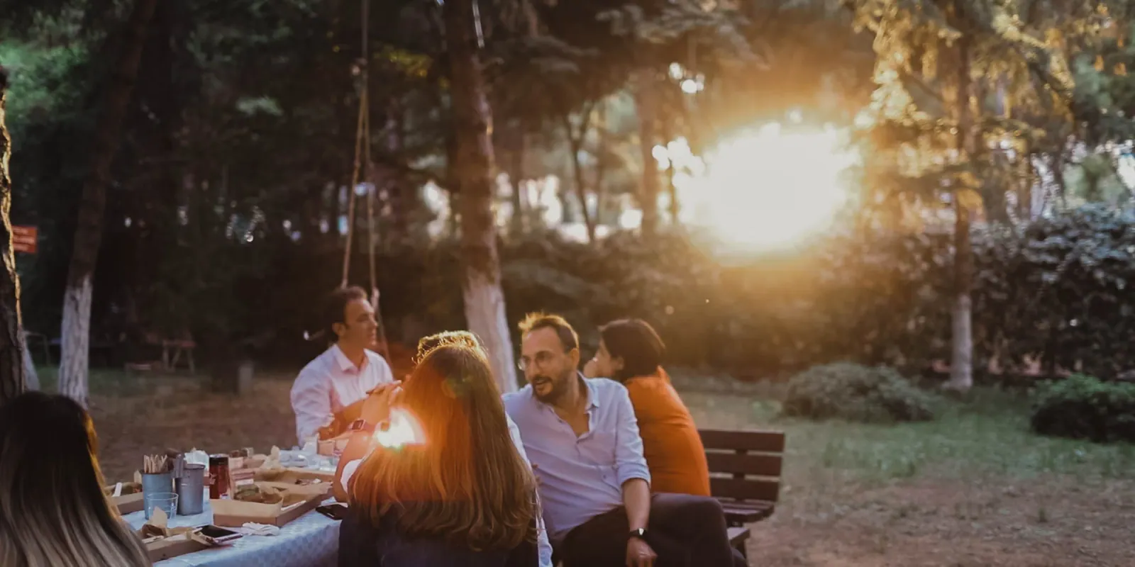 The OmmaWorks team sharing a meal outdoors at a company gathering in a pine forest at golden hour