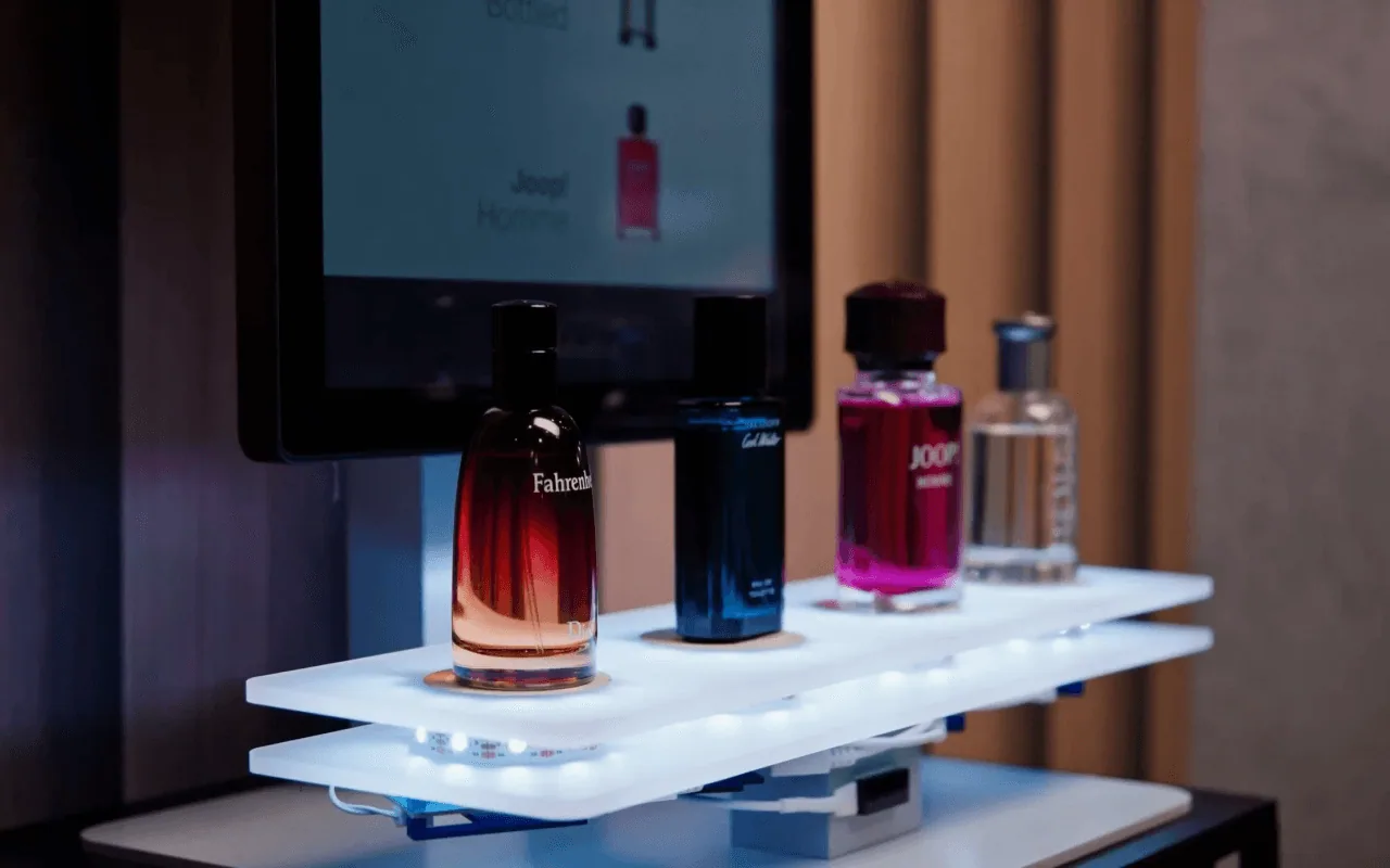 Fragrance bottles on an illuminated Nexmosphere lift-and-learn sensor shelf in front of a screen